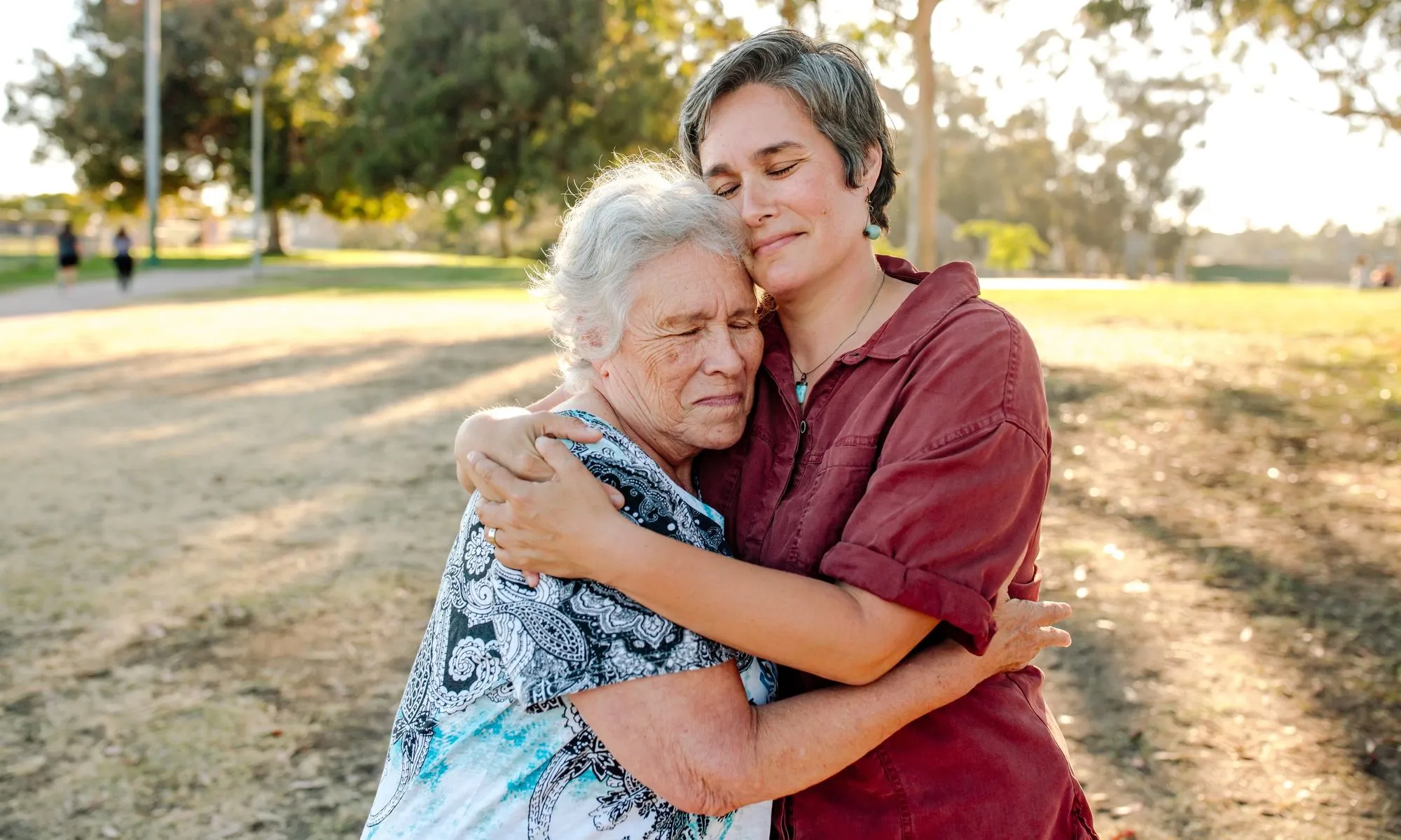 An adult daughter and mother hug in a park