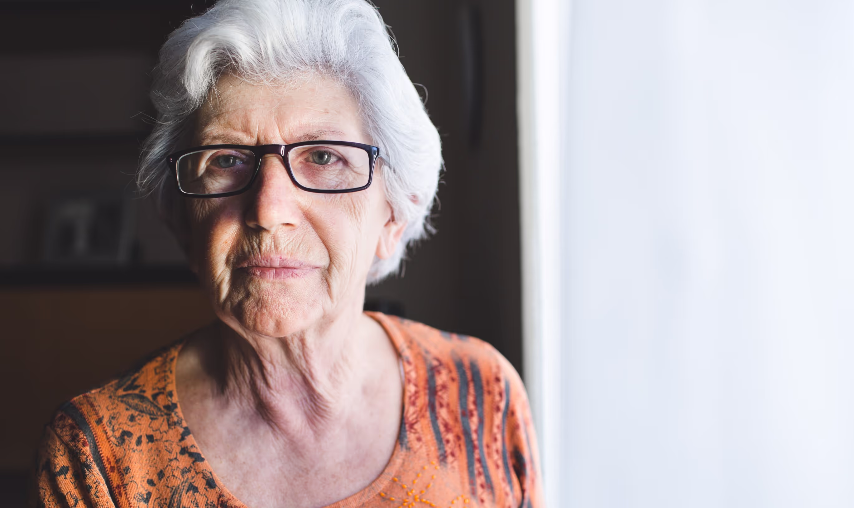 Grey-haired woman near window looks dramatically at camera