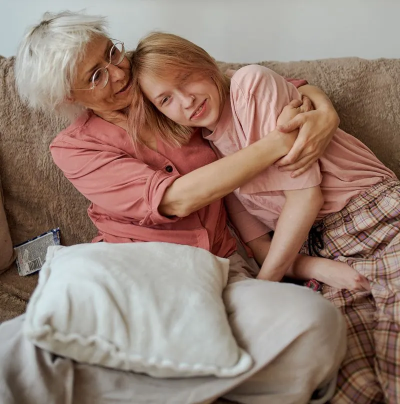 Gray-haired woman hugs her granddaughter on the couch