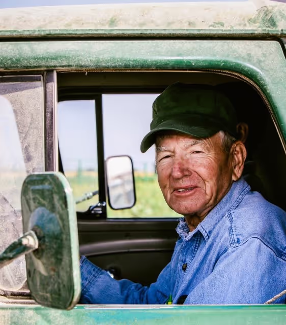 Weathered farmer smiles from dusty pickup truck