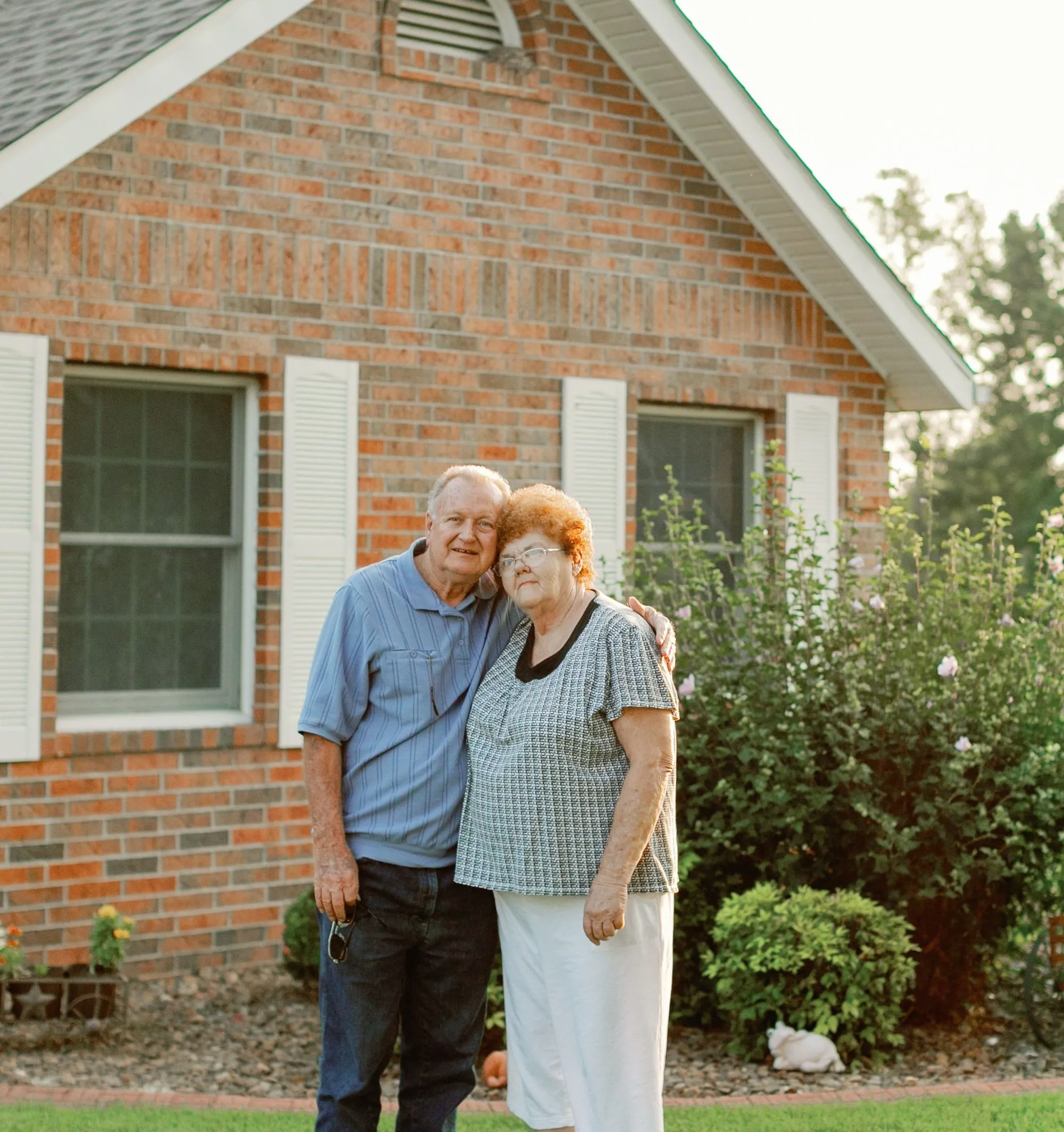 Elderly couple embraces outside home